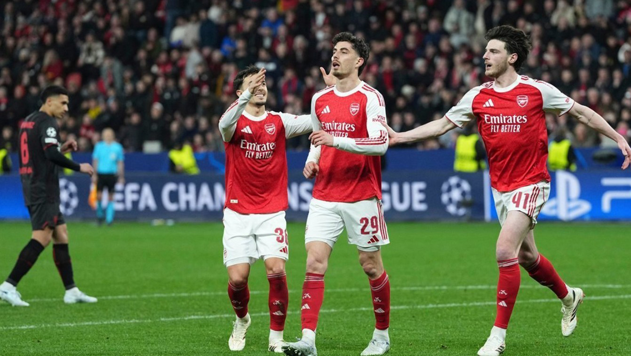 Tiga pemain Arsenal, termasuk Kai Havertz dan Declan Rice, merayakan gol di lapangan saat pertandingan Liga Champions melawan Bayer Leverkusen.