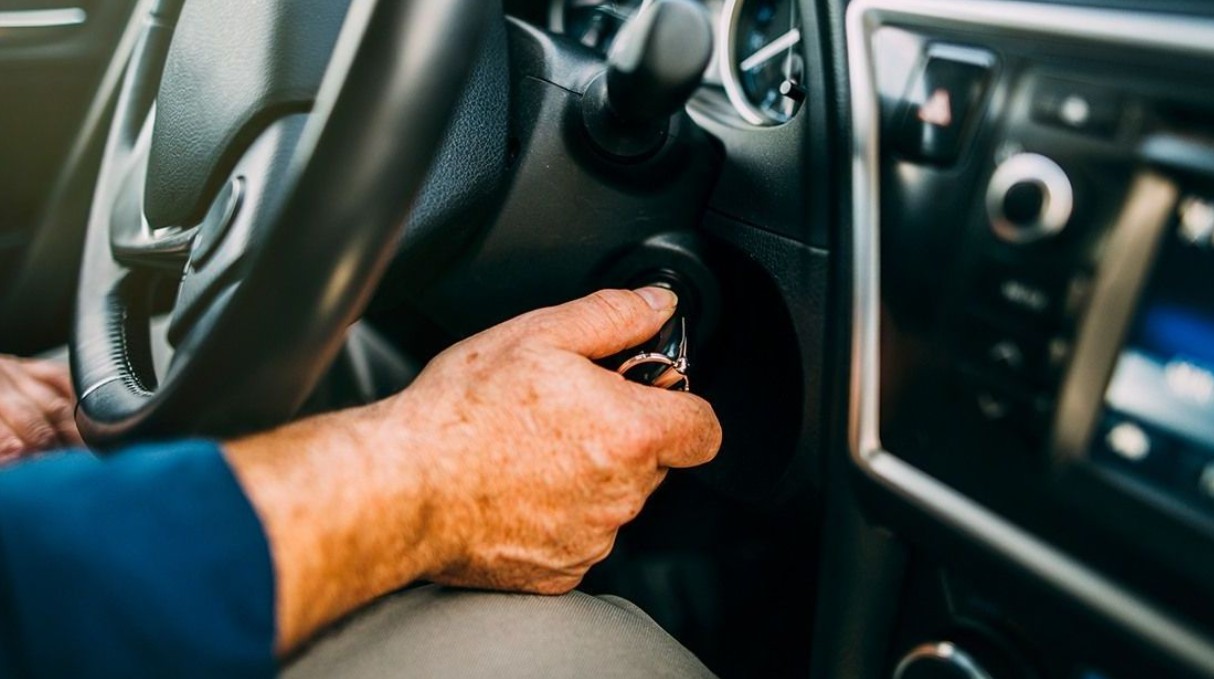 Tangan seorang pengemudi sedang memegang dan memutar kunci kontak di dalam lubang kunci dasbor mobil untuk menyalakan atau mematikan mesin.