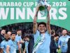 pemain muda Manchester City dengan banyak tato di lengan, Nico O'Reilly, merayakan kemenangan sendirian di depan spanduk panggung bertuliskan "CARABAO CUP FINAL 2026 WINNERS".