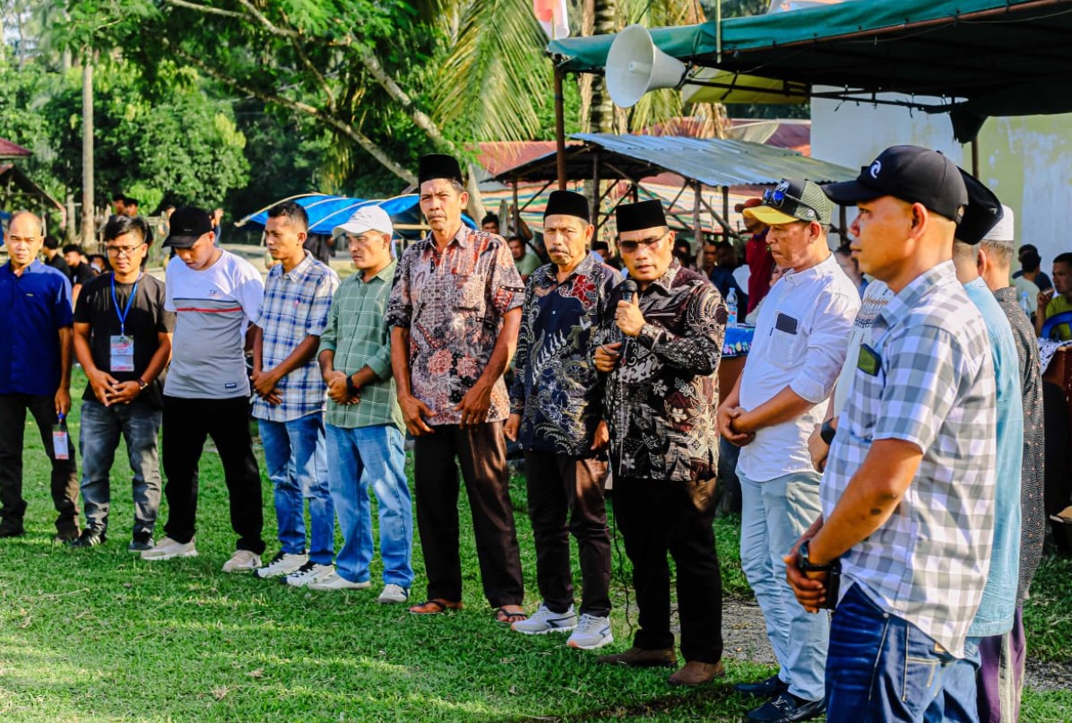 Camat Halongonan Timur memegang mikrofon dan memberikan sambutan kepada pejabat desa di bawah tenda panggung.