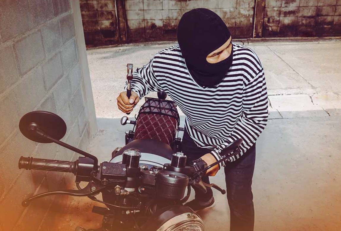 Seorang pencuri sepeda motor bertopeng menggunakan palu untuk membobol sepeda motor kustom di sebuah gang beton.