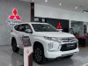 Sebuah foto close-up depan-samping dari Mitsubishi Pajero Sport Facelift 2026 berwarna putih yang dipajang di showroom Mitsubishi Motors modern, menampilkan desain boxy baru dan lampu T-Shaped.