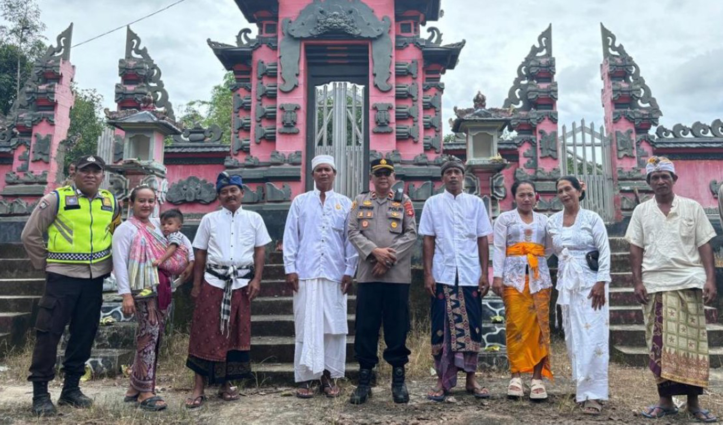 Sebuah foto kelompok yang menunjukkan petugas polisi dan warga Bali berdiri di depan pura Hindu Bali yang besar.