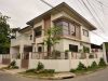 Rumah hook 2 lantai bergaya modern tropis dengan fasad putih dan aksen kayu, menampilkan jendela sudut besar dan pagar minimalis.