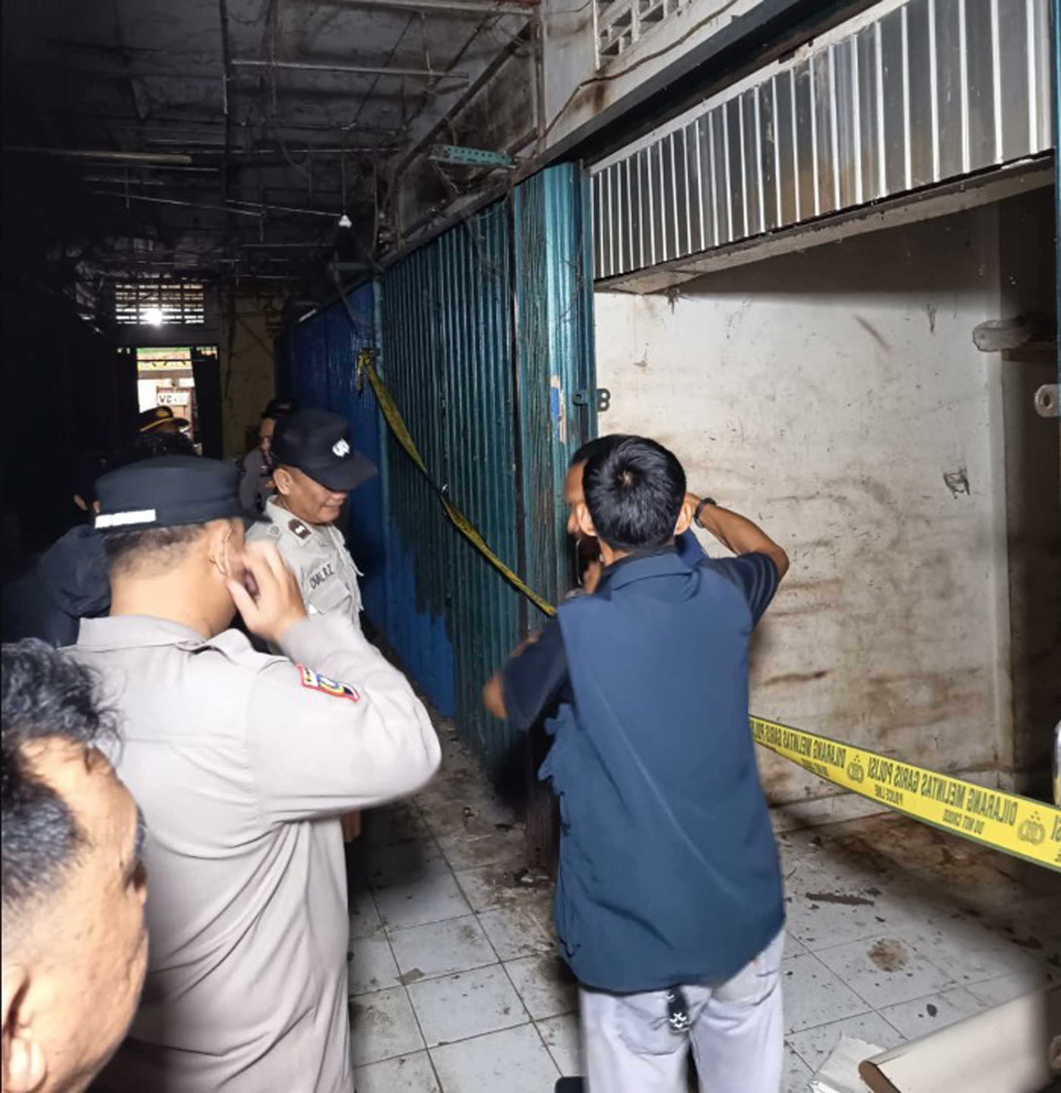 Aparat kepolisian Polsek Baturaja Timur memeriksa gembok kios tertutup di Pasar Atas OKU menggunakan senter.