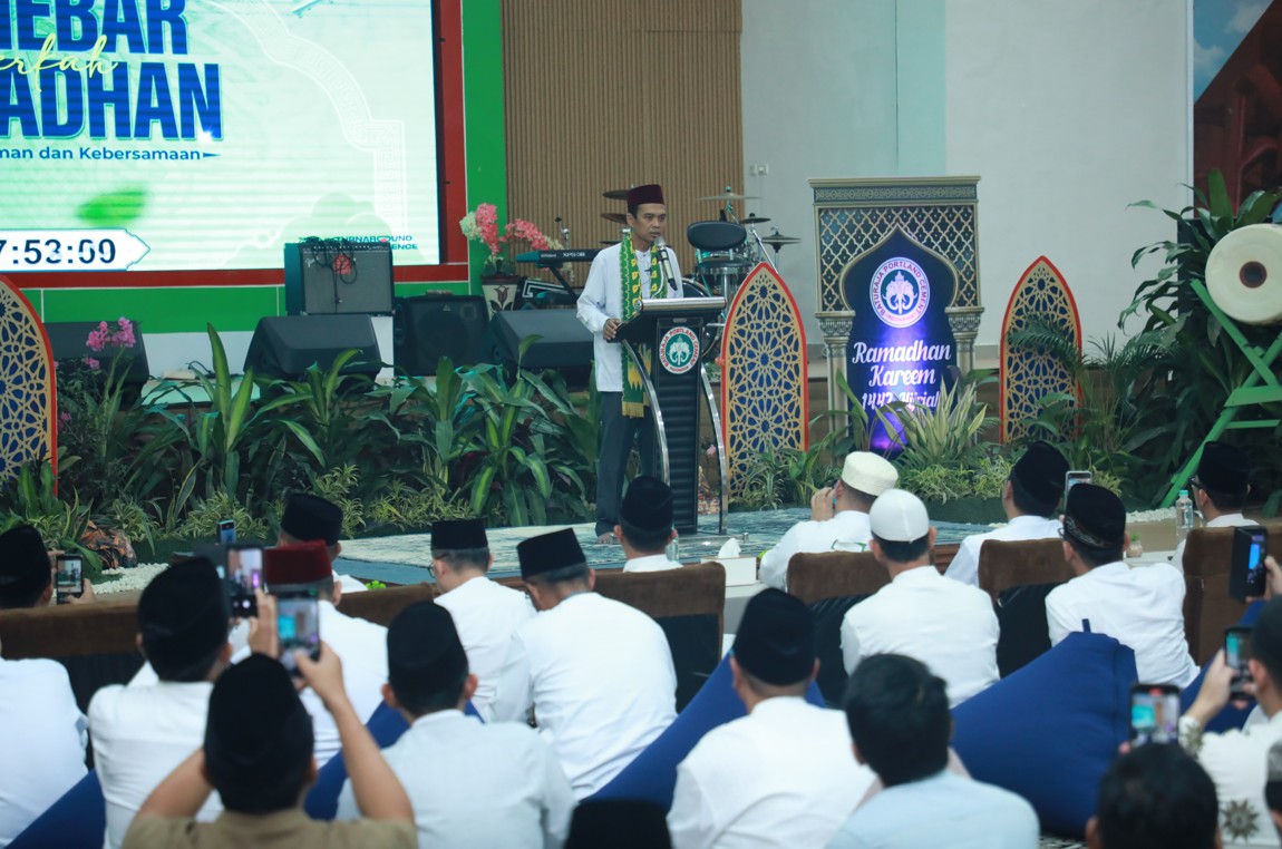 Ustadz Abdul Somad berdiri di atas mimbar menyampaikan ceramah agama di depan latar layar bertuliskan Ramadan, sementara jamaah berpakaian putih duduk khusyuk mendengarkan.
