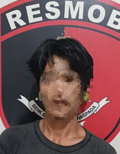 oto penahanan (mugshot) seorang pria berambut hitam berdiri di depan logo Kepolisian Indonesia 'RESMOB', dengan wajah yang disamarkan (pixelated), mengenakan kaus gelap.