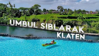 Wisatawan bersantai memakai pelampung kuning di kolam biru Umbul Siblarak Klaten berlatar hamparan sawah