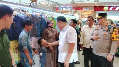 Wakil Bupati OKU Marjito Bachri menyapa dagu seorang anak kecil di dalam Citimall Baturaja. Ia didampingi Kapolres OKU AKBP Endro Aribowo. Latar belakang menampilkan lorong mall dengan rak pakaian.