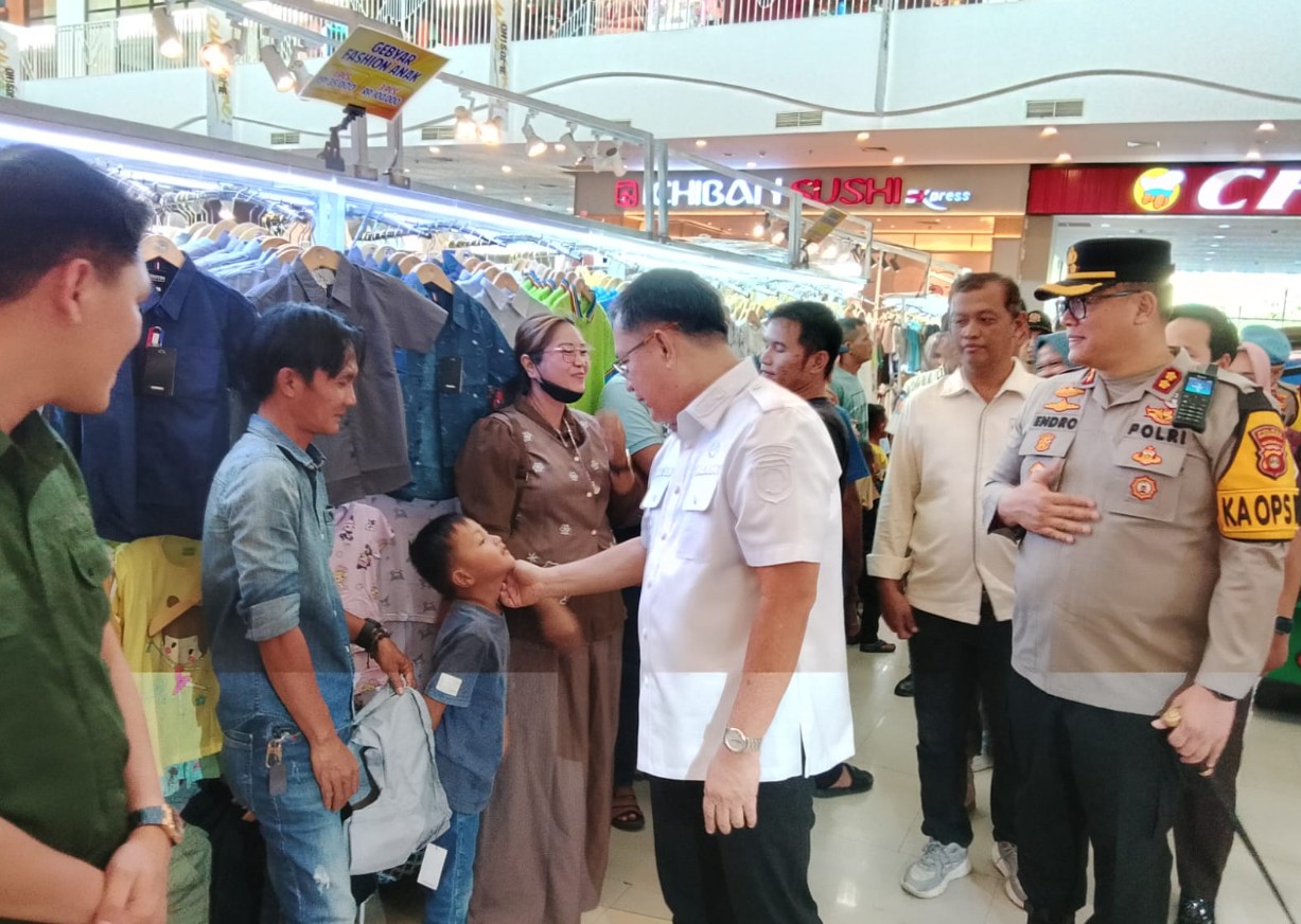 Wakil Bupati OKU Marjito Bachri menyapa dagu seorang anak kecil di dalam Citimall Baturaja. Ia didampingi Kapolres OKU AKBP Endro Aribowo. Latar belakang menampilkan lorong mall dengan rak pakaian.