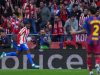 Seorang pemain sepak bola Atletico Madrid (Ademola Lookman, jersey no. 22) berlari dan berteriak merayakan gol di hadapan pendukung yang bersorak. João Cancelo dari Barcelona (jersey no. 2) berdiri di latar depan dengan punggung menghadap kamera, tampak kecewa. Papan iklan LED terlihat.