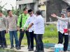 Foto outdoor sekelompok orang, dipimpin oleh Bupati OKU Teddy Meilwansyah yang mengenakan kemeja putih 'BUPATI', sedang meninjau kolam budidaya ikan dengan keramba logam di BBPAT Sukabumi. Seorang staf teknis sedang menunjuk ke kolam.