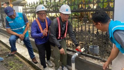 Bupati OKU Teddy Meilwansyah dan Dirut PDAM Bertho Darmo memutar katup pipa air di samping pagar hitam.