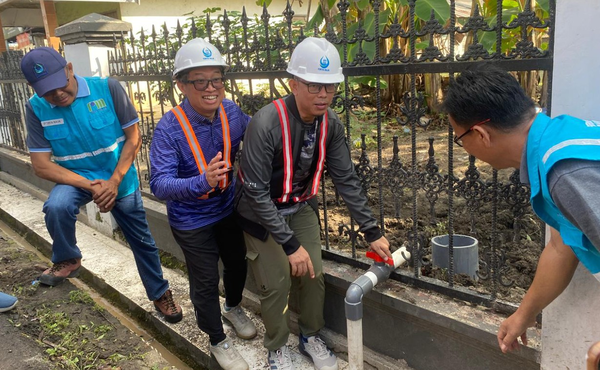 Bupati OKU Teddy Meilwansyah dan Dirut PDAM Bertho Darmo memutar katup pipa air di samping pagar hitam.