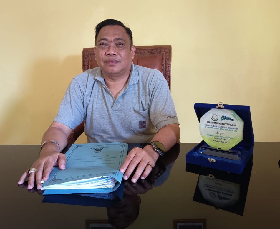 Potret Direktur Perumda Pasar OKU Radius Susanto duduk di meja kerja membawa dokumen perjanjian sewa kios Pasar Atas Baturaja.