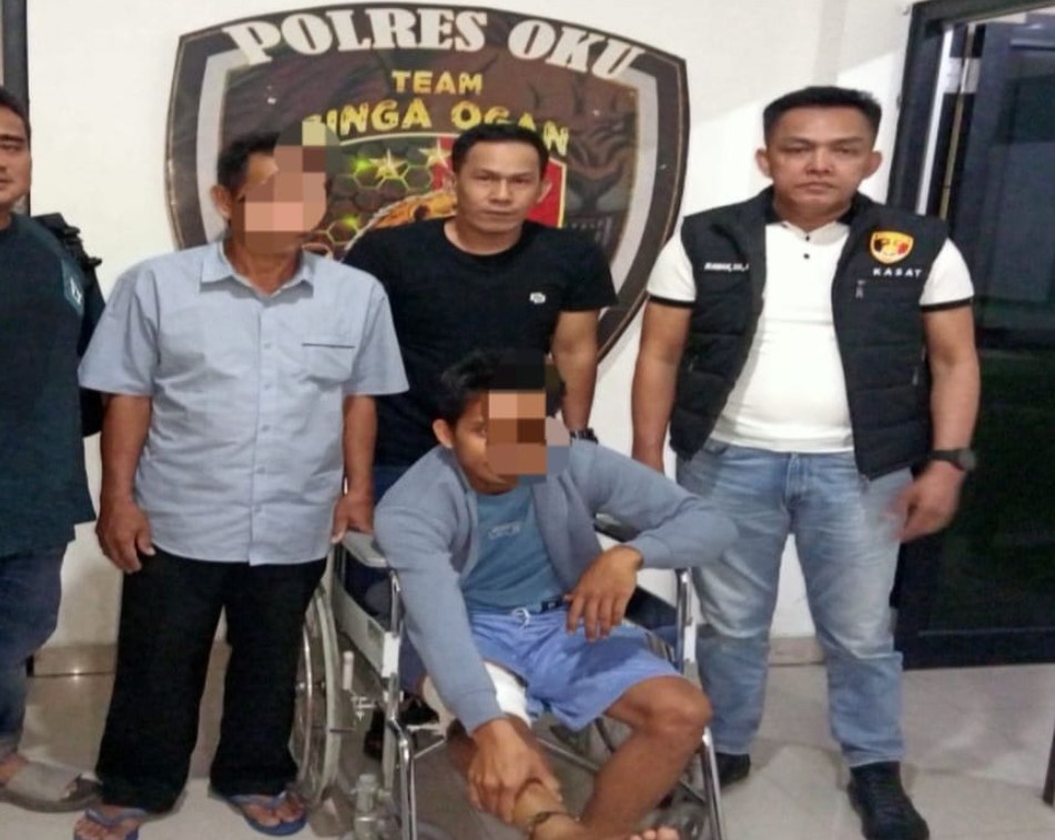 Foto bersama di depan logo Polres OKU Team Singa Ogan. Lima pria berpose, di mana Kasat Reskrim AKP Irawan Adi Candra di kanan berompi taktis hitam "KASAT". Di tengah duduk tersangka di kursi roda kaki kiri dibalut perban putih, didampingi tersangka lain dan polisi.