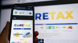 Tampilan layar ponsel pintar yang sedang membuka situs web Coretax DJP untuk pelaporan SPT Tahunan dengan latar belakang monitor komputer.