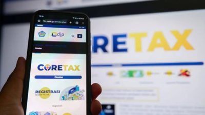 Tampilan layar ponsel pintar yang sedang membuka situs web Coretax DJP untuk pelaporan SPT Tahunan dengan latar belakang monitor komputer.