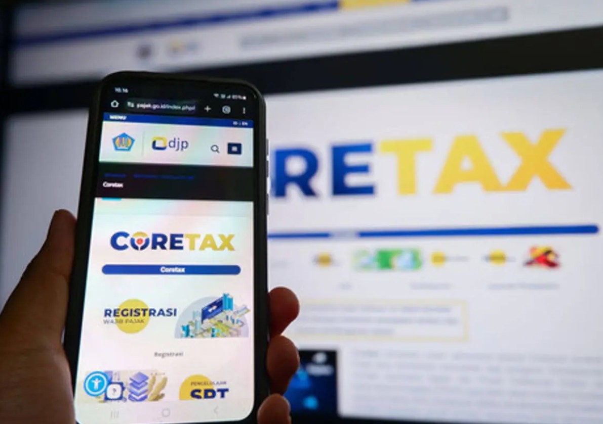 Tampilan layar ponsel pintar yang sedang membuka situs web Coretax DJP untuk pelaporan SPT Tahunan dengan latar belakang monitor komputer.