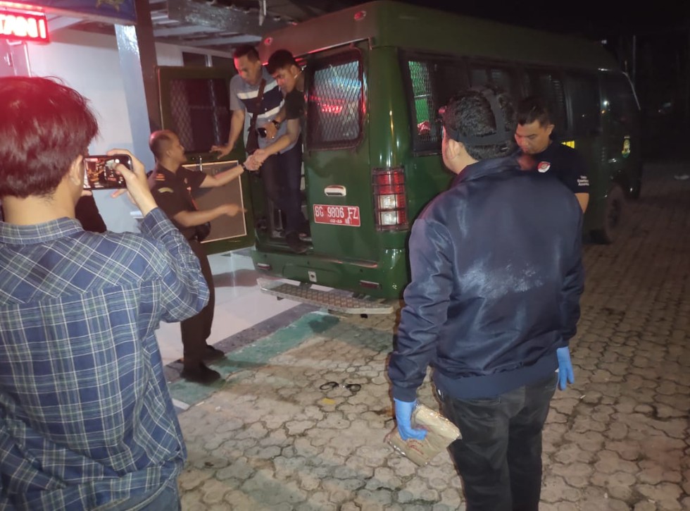 Petugas kepolisian dan jaksa memeriksa mobil tahanan hijau BG 9806 FZ di depan Rutan Baturaja saat malam hari terkait insiden tahanan kabur.