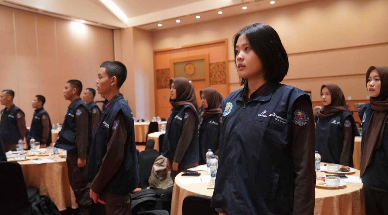 Mahasiswa penerima beasiswa PHR Zona 4 berseragam rompi biru sedang berdiri tegak di ruang pertemuan.