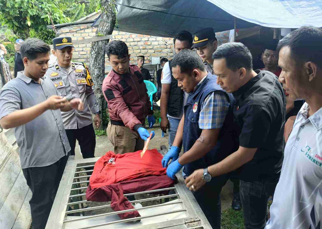 Gambar sekelompok polisi dan warga berkumpul di sekitar meja logam di halaman luar. Seorang petugas dengan sarung tangan biru menunjuk ke kemeja merah di atas meja.