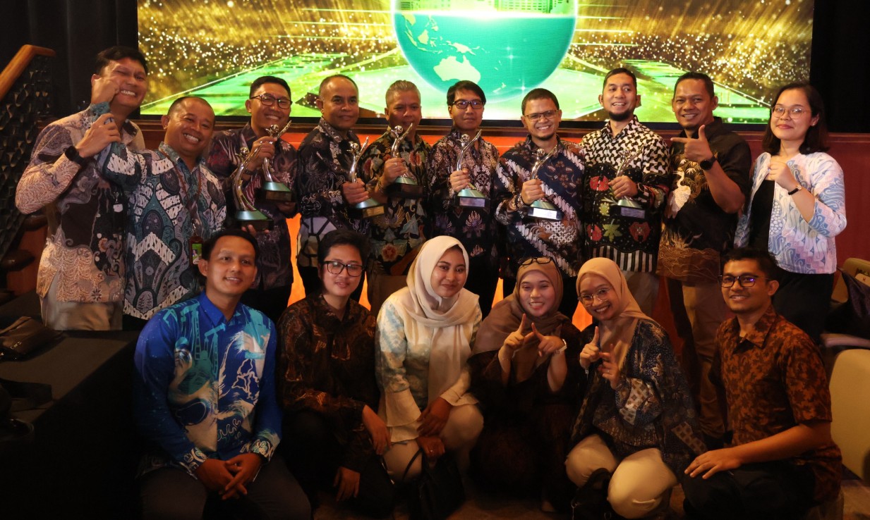 Sekelompok staf Pertamina PEP Zona 4 tersenyum gembira memegang trofi PROPER di panggung penghargaan yang meriah.
