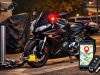 Foto malam hari sebuah sepeda motor sport hitam dan merah diparkir dengan rantai dan kunci cakram terpasang. Sebuah smartphone di latar depan menampilkan aplikasi pelacakan GPS dengan pin lokasi, dengan kunci kontak dan remote fob di sampingnya.