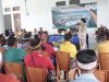 Bupati Sumba Barat Daya, Ratu Ngadu Bonnu Wulla menyampaikan kepada warga latar belakang bertuliskan 'SOSIALISASI PENANGANAN LONG SEGMEN JALAN OMBARADE - KALIMBU TILLU'. Audiens difoto dari belakang, beberapa mengenakan penutup kepala tradisional Sumba. Latar belakangnya adalah bangunan semi-terbuka dengan tanaman hias.