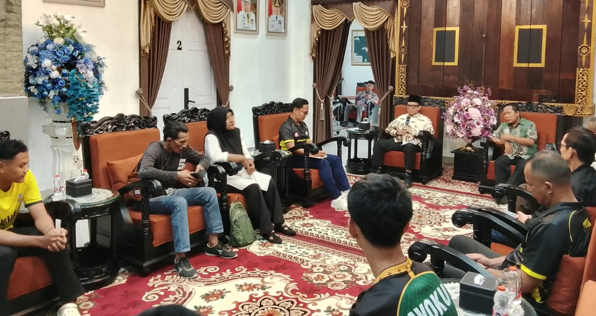 Bupati OKU Teddy Meilwansyah berbaju batik formal duduk memberikan motivasi kepada tim voli muda AVOKU (baju olahraga hijau dan kuning) yang duduk di hadapannya di ruang tamu formal pendopo rumah dinas.