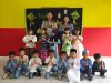 Sekelompok siswa dan dua guru berpose salam namaste di depan dekorasi panggung Halal Bihalal.
