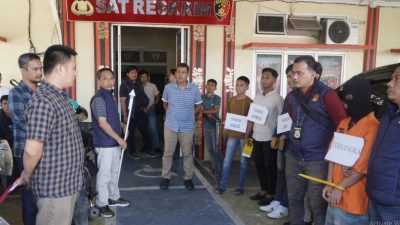 Tersangka berbaju oranye dan sejumlah saksi memegang papan nama saat proses rekonstruksi kasus pembunuhan Desa Pelangki di depan kantor Sat Reskrim Polres OKU Selatan.