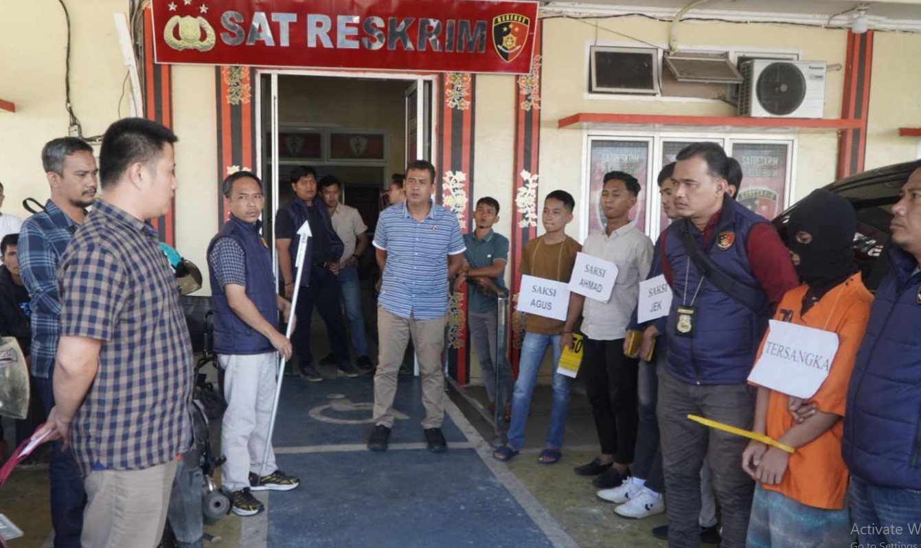 Tersangka berbaju oranye dan sejumlah saksi memegang papan nama saat proses rekonstruksi kasus pembunuhan Desa Pelangki di depan kantor Sat Reskrim Polres OKU Selatan.