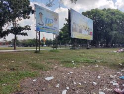 A photo of an open park area in Indonesia with two large metal-framed billboards in the background, featuring photos of officials and text commemorating Indonesian events, with plastic trash scattered across the grass in the foreground under a cloudy sky, dated June 29, 2026.