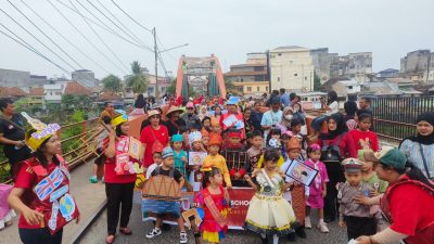 Rombongan pawai TK SD Xaverius Global School mengenakan kostum budaya dan profesi melintasi Jembatan Ogan Baturaja.