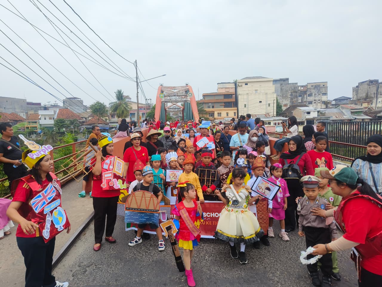 Rombongan pawai TK SD Xaverius Global School mengenakan kostum budaya dan profesi melintasi Jembatan Ogan Baturaja.