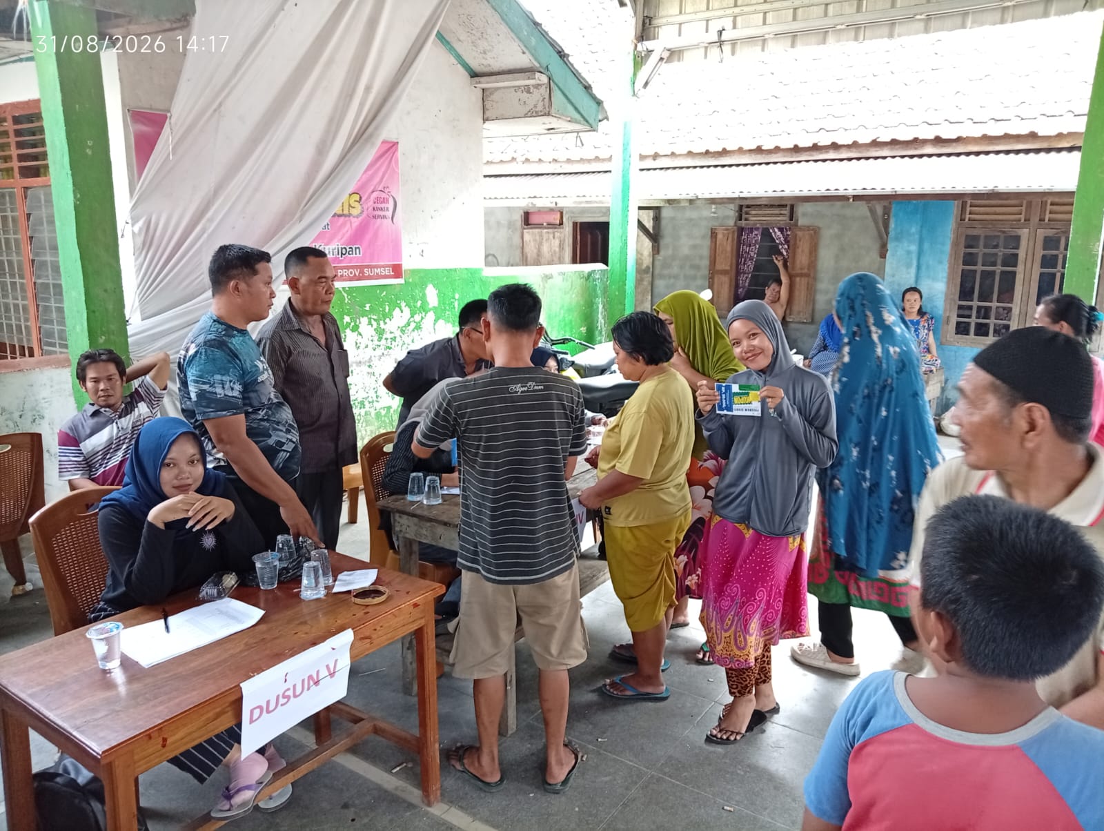Suasana antrean warga di meja pendaftaran Dusun V dengan seorang wanita menunjukkan kupon Program SEHATI.