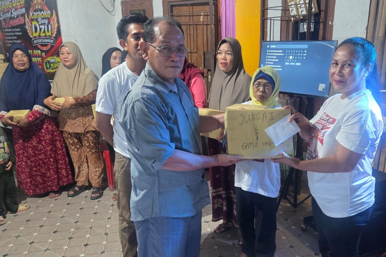 Ketua Panitia Pemilihan BPD Tanjung Kemala berkacamata menyerahkan kotak hadiah lomba kepada ibu-ibu warga setempat.