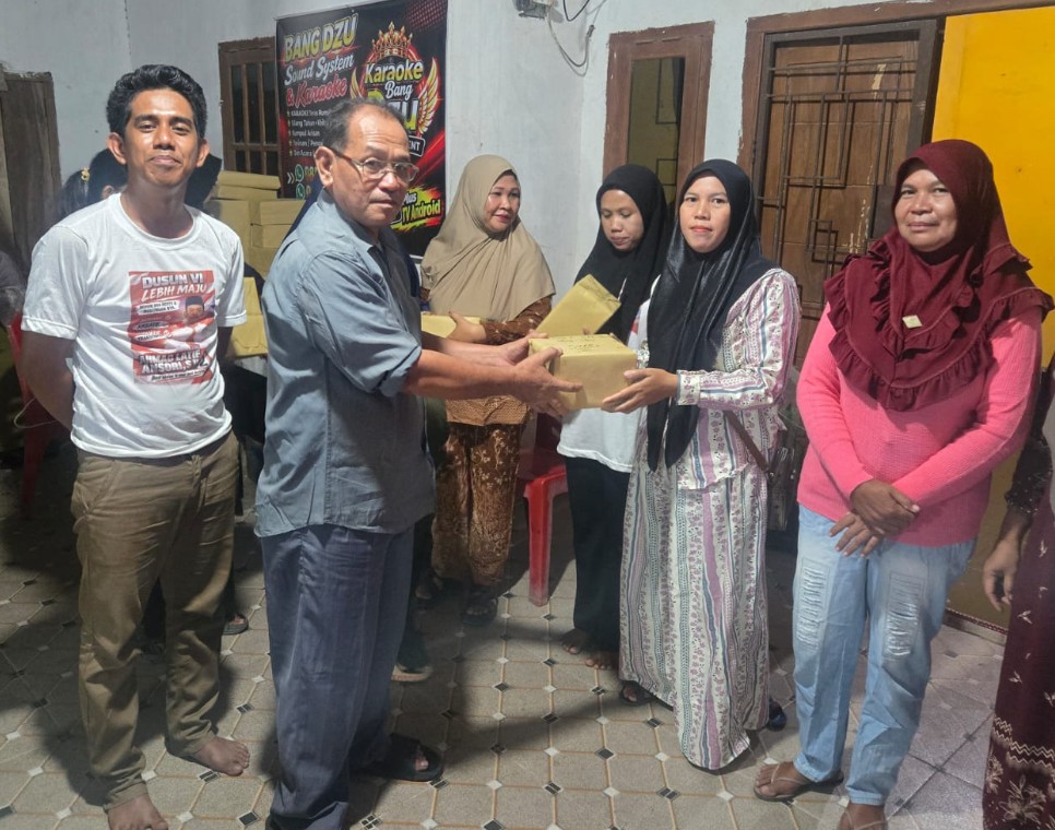 Ketua Panitia Pemilihan BPD Tanjung Kemala berkacamata menyerahkan kotak hadiah lomba kepada ibu-ibu warga setempat.