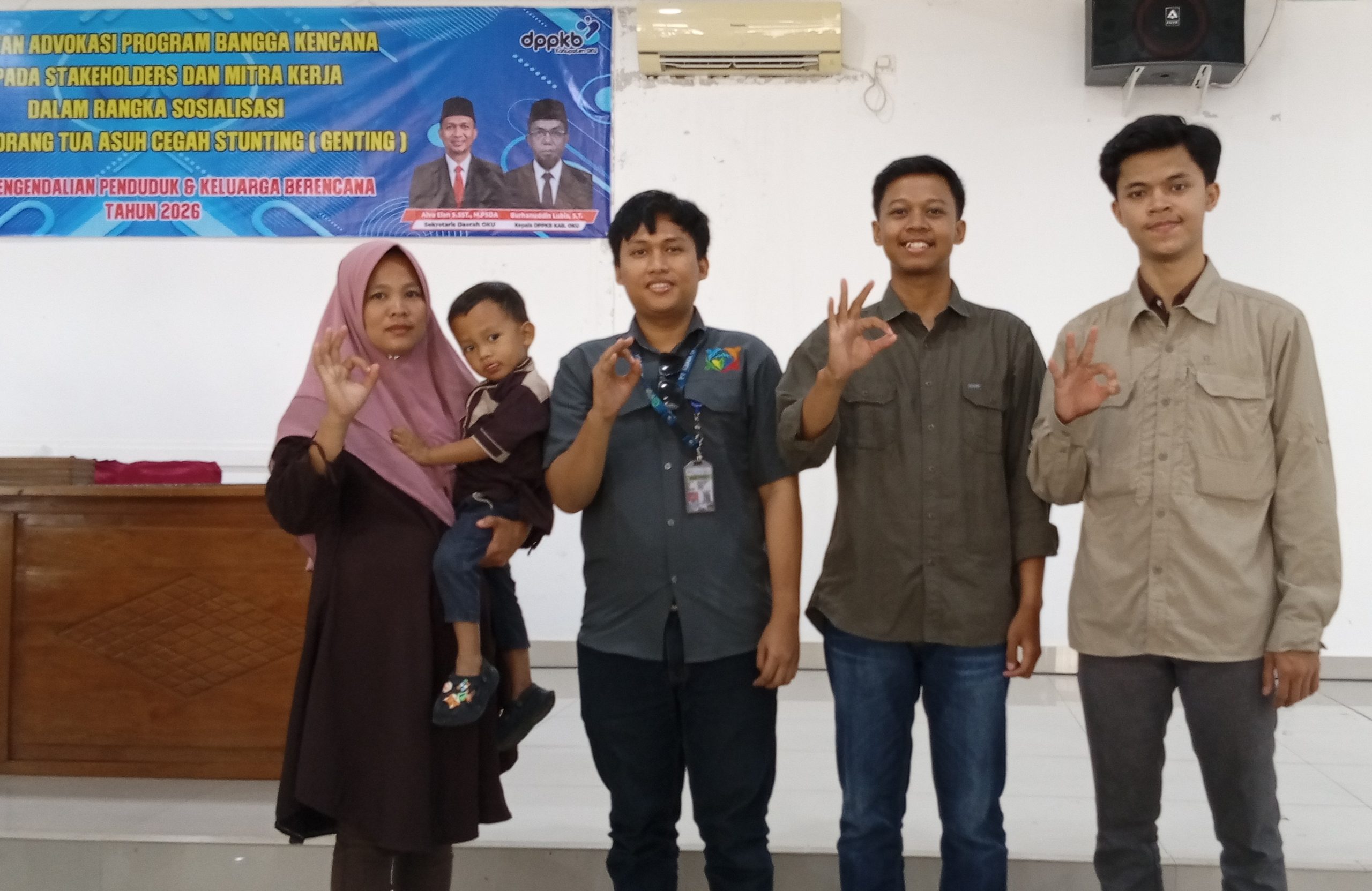 Tiga perwakilan perusahaan berfoto bersama ibu dan balita penerima bantuan gizi sambil menunjukkan gestur jari OK.