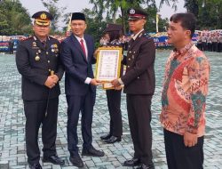 Sekda OKU Alva Elan dan Kapolres OKU AKBP Endro Aribowo menyerahkan piagam penghargaan bertingkai emas kepada seorang anggota kepolisian pada Upacara Hari Bhayangkara ke-80 di Mapolres OKU.