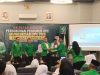 Kader Partai Kebangkitan Bangsa berseragam hijau saling menyerahkan dokumen di atas panggung dengan latar spanduk Muskercab DPC PKB Kabupaten OKU.