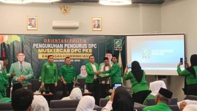 Kader Partai Kebangkitan Bangsa berseragam hijau saling menyerahkan dokumen di atas panggung dengan latar spanduk Muskercab DPC PKB Kabupaten OKU.
