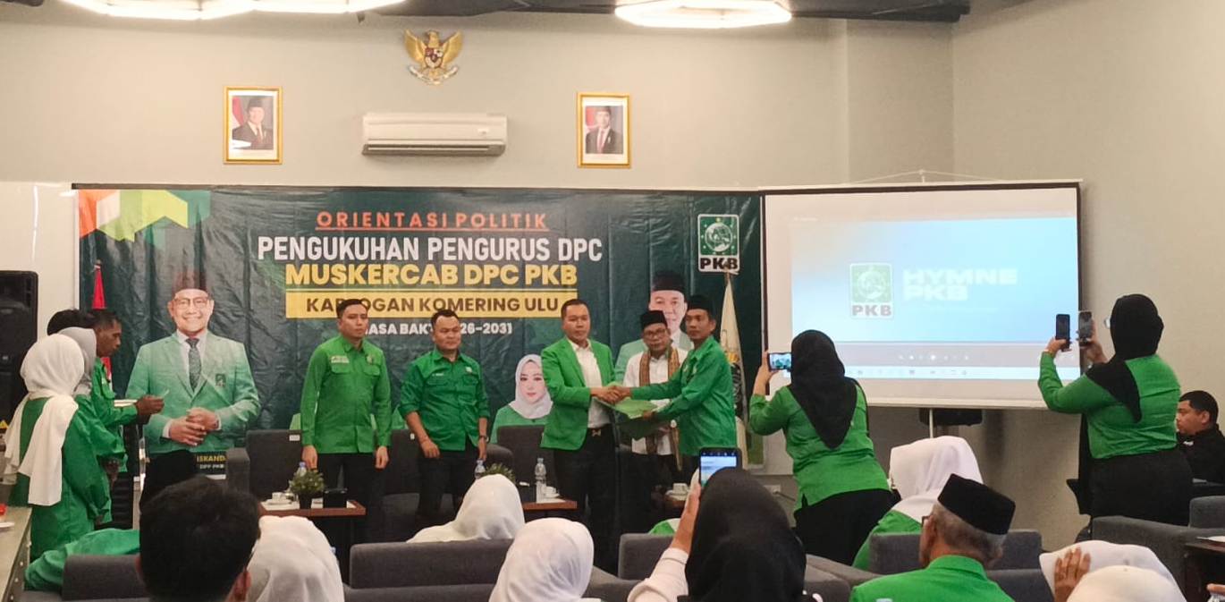 Kader Partai Kebangkitan Bangsa berseragam hijau saling menyerahkan dokumen di atas panggung dengan latar spanduk Muskercab DPC PKB Kabupaten OKU.