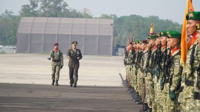 Inspektur upacara militer berjalan memeriksa barisan prajurit TNI bersenjata.